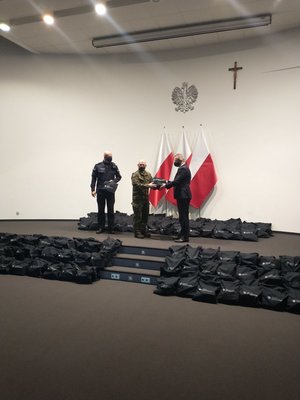 Mężczyzna przekazuje paczkę żołnierzowi na tle rozłożonych na podłodze paczek