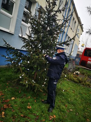 Policjant przy choince ubranej w elementy odblaskowe przy budynku komendy Policji