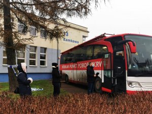 Policjanci stojący w kolejce do ambulansu krwiodawstwa przed budynkiem komendy