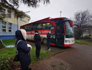 Policjanci stojący w kolejce do ambulansu krwiodawstwa przed budynkiem komendy