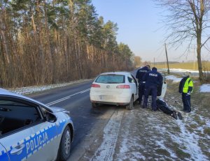 Zatrzymanie sprawców przestępstw i wykroczeń. Pojazd stojący na poboczu, przy nim trzech policjantów oraz radiowóz