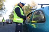 Policjant stojący przy niebieskim samochodzie i badający trzeźwość kierowcy