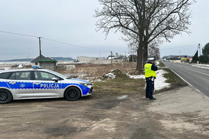 policjant umundurowany stojący obok oznakowanego radiowozu